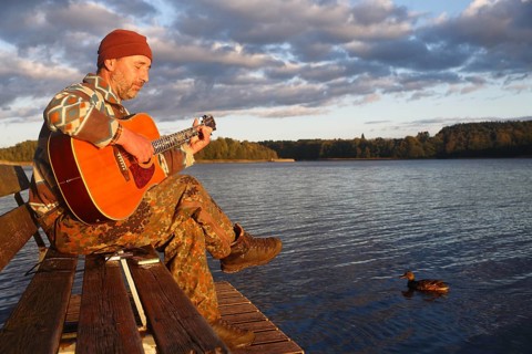 Man playing guitar on a jetty by the lake