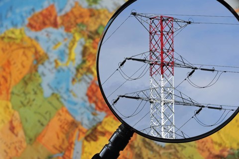 High voltage pylon in red and white through magnifying glass held against illuminated terrestrial globe