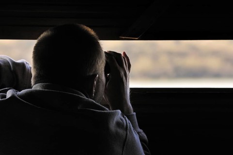 Bird watcher in hide looking through binoculars at waterfowl on lake in the nature reserve Parc du Marquenterre at the Bay of the Somme