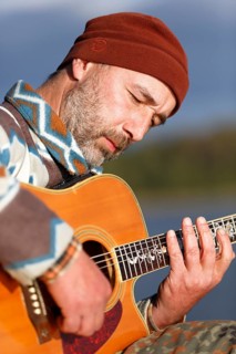 Man playing guitar on a jetty by the lake