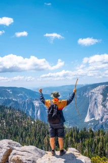 A young man with a walking stick and arms raised at Sentinel Dome in Yosemite National Park. United States