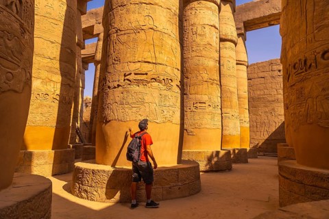 A young tourist walking among the columns with hieroglyphs inside the Karnak Temple