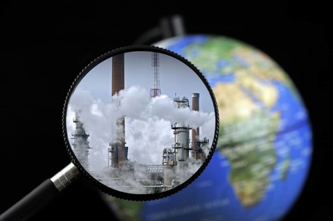 Chimneys covered in smoke seen through magnifying glass held against illuminated terrestrial globe