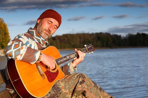 Man playing guitar on a jetty by the lake