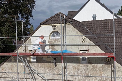 Painter on scaffolding plastering the facade of a house from 1830