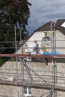 Painter on scaffolding plastering the facade of a house from 1830