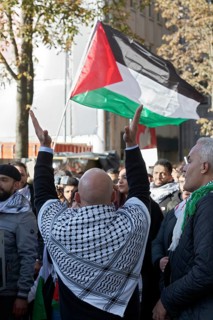 Demo participant with Palestinian scarf claps hands