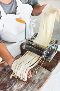 Close up baker cutting raw dough into tagliatelle pasta machine