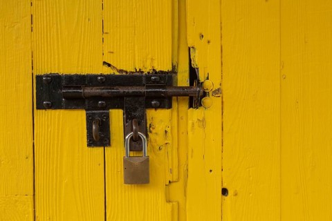 Yellow painted wood plank barn door locked with brass padlock
