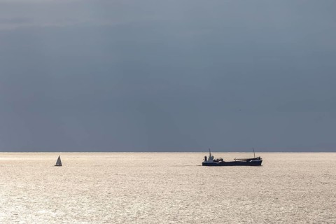 Dark clouds and sunlight and a sailboat and freighter over the North Sea