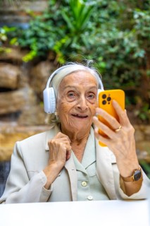 Vertical portrait of a elder woman listening to music using phone in a geriatric