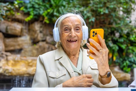 Happy elder woman using headphones and mobile to listening to music in a geriatric