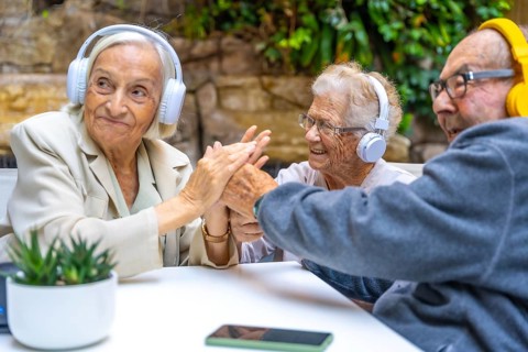 Seniors enjoying music using headphones sitting on a garden in a nursing home