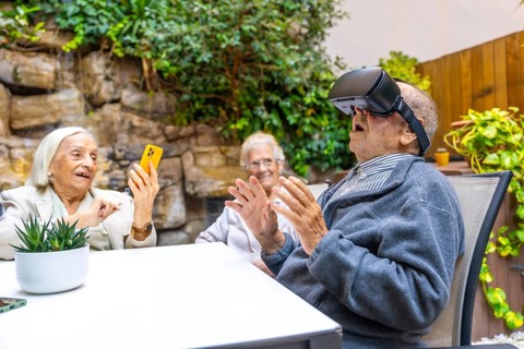 Elder man using virtual reality goggles sitting on the garden of a nursing home