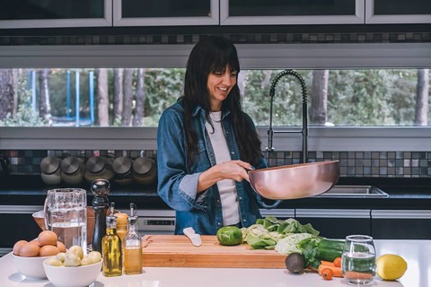 A woman cooking vegetables in a copper wok