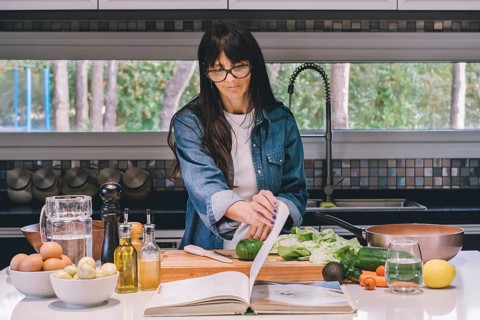 Mid-adult woman reading recipe while preparing food in the kitchen