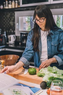 Mid-adult woman reading recipe while preparing food in the kitchen. Vertical shot