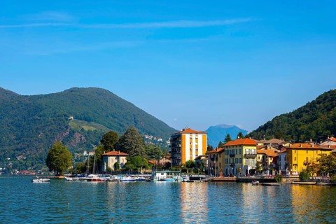 City of Porto Ceresio on Waterfront with Mountain and Lake Lugano in a Sunny Summer Day in Porto Ceresio