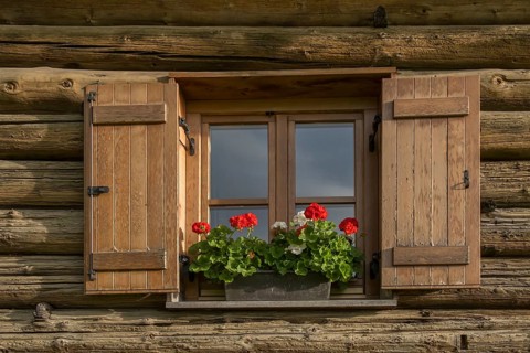 Window with shutters and geraniums at an alpine hut