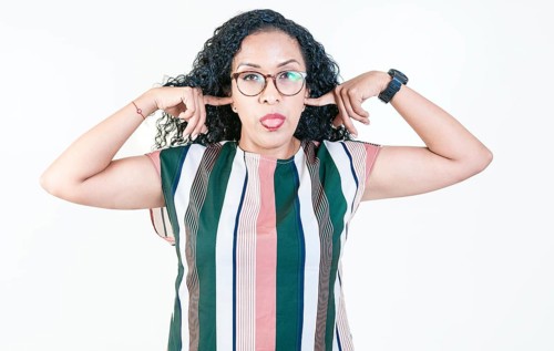 Displeased afro woman covering ears and sticking out tongue isolated. Latin woman covering her ears and making faces isolated