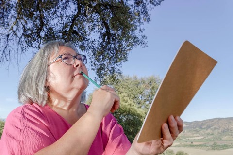 Older white-haired woman with a pencil on her lips and a notebook in her hand