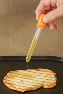 Woman pours olive oil on toast with an dropper because of excessive oil prices