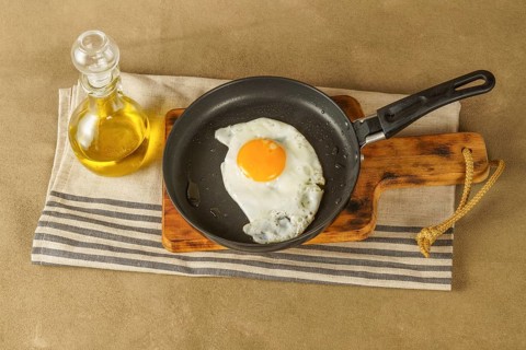 Fried egg with extra virgin olive oil in a frying pan with a glass bottle with oil on a wooden board