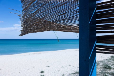 Straw mat hanging in the wind on a hut on a white sandy beach in front of a bright blue sea