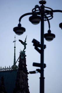 Angel figure with sword on the roof of the town hall fighting against a pole with lamps and video cameras