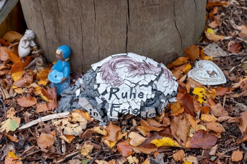 Mementos and stones in the shape of a heart on a memorial tree with the names of the buried