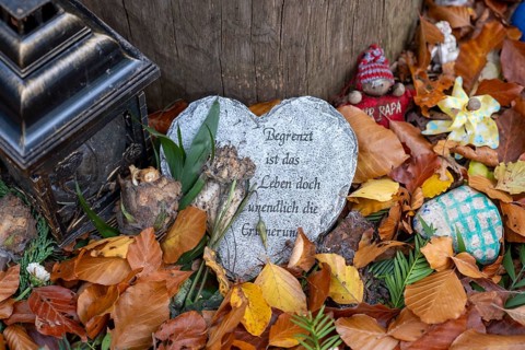Mementos and stones in the shape of a heart on a memorial tree with the names of the buried