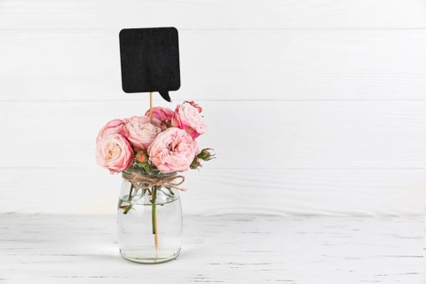 Black speech bubble prop rose glass jar against white wooden backdrop