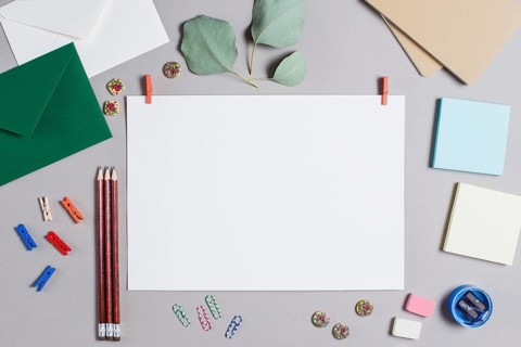 Blank white page with clothes peg surrounded with stationeries gray background
