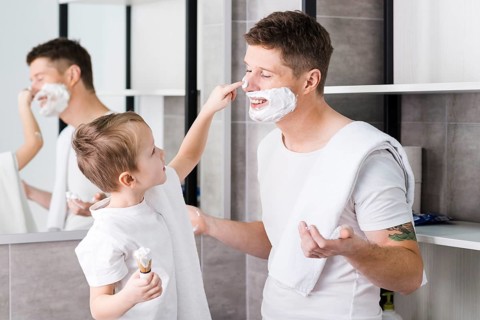 Close up boy applying shaving foam his father s face bathroom