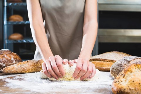 Close up female baker kneading dough with flour wooden surface