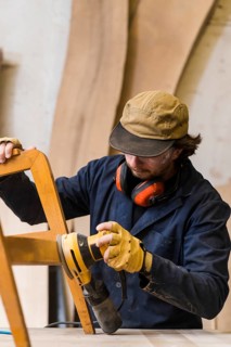 Close up male carpenter sanding furniture with power tool workbench