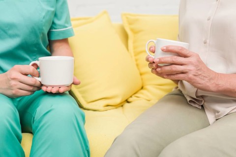 Close up nurse patient sitting sofa holding coffee cups