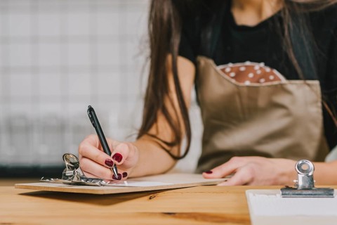 Crop waitress writing clipboard