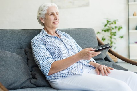 Elderly woman watching television using remote