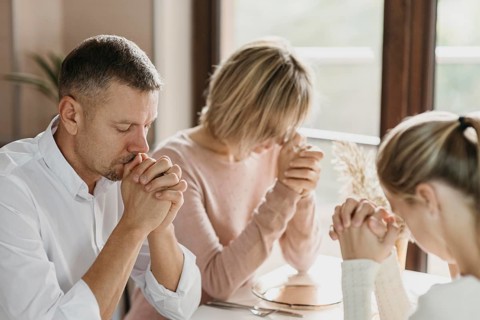 Family praying together before eating indoors