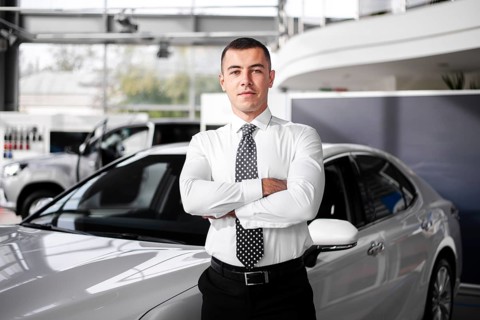 Front view male car dealer standing with arms crossed