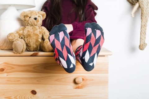 Girl sitting near soft toy showing her feet with multi colored socks