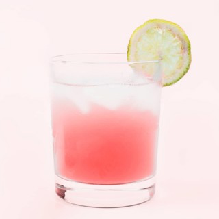 Glass cocktail drink with lemon slice against pink background