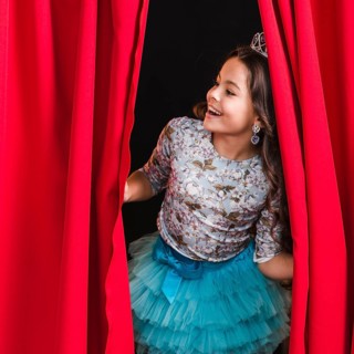 Happy girl peeking from red curtain stage
