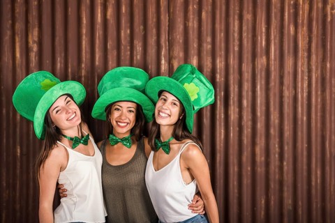 Happy young women saint patricks hats embracing near wall