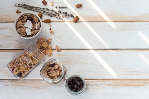 Jar spilled granola near cornflakes dry fruits chocolate chips wooden plank