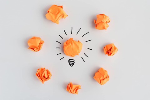 Light bulb with crumpled colorful paper white surface