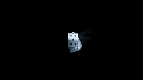 Magician s hand showing club playing card against black background