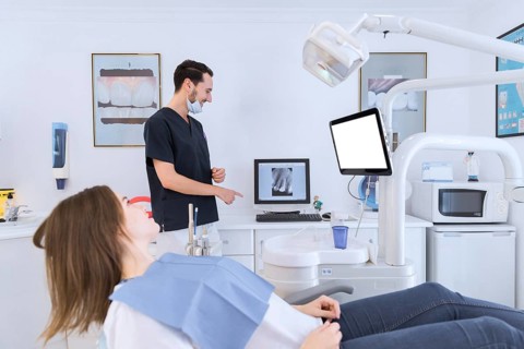 Male dentist explaining teeth x ray screen female patient lying dentist chair