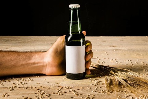 Man s hand holding beer bottle with ears wheat wooden surface